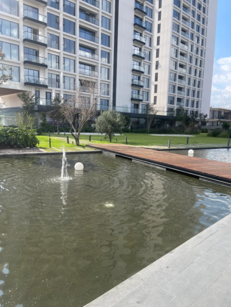 Espejo de agua con fuentes y deck de madera en las áreas comunes del conjunto